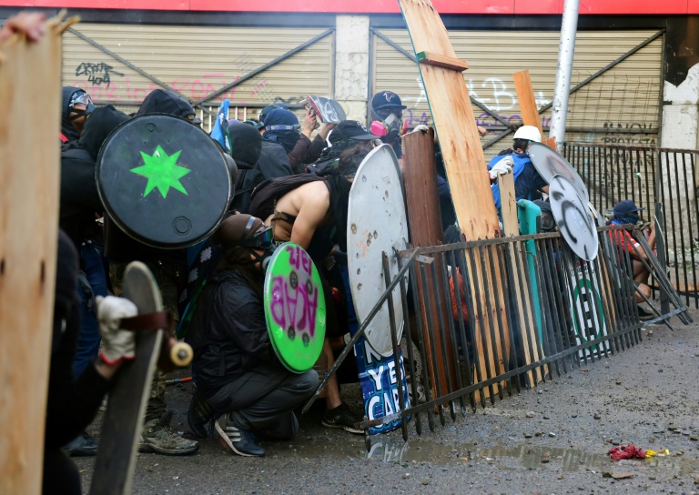 Des manifestants se protègent face aux forces de l'ordre à Santiago, hier vendredi